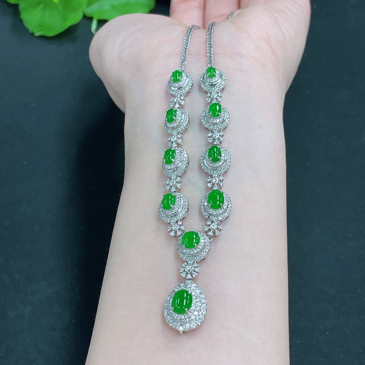Huiliu Jadeite necklace set with diamonds featuring a polished jade pendant and matching earrings on a display stand.