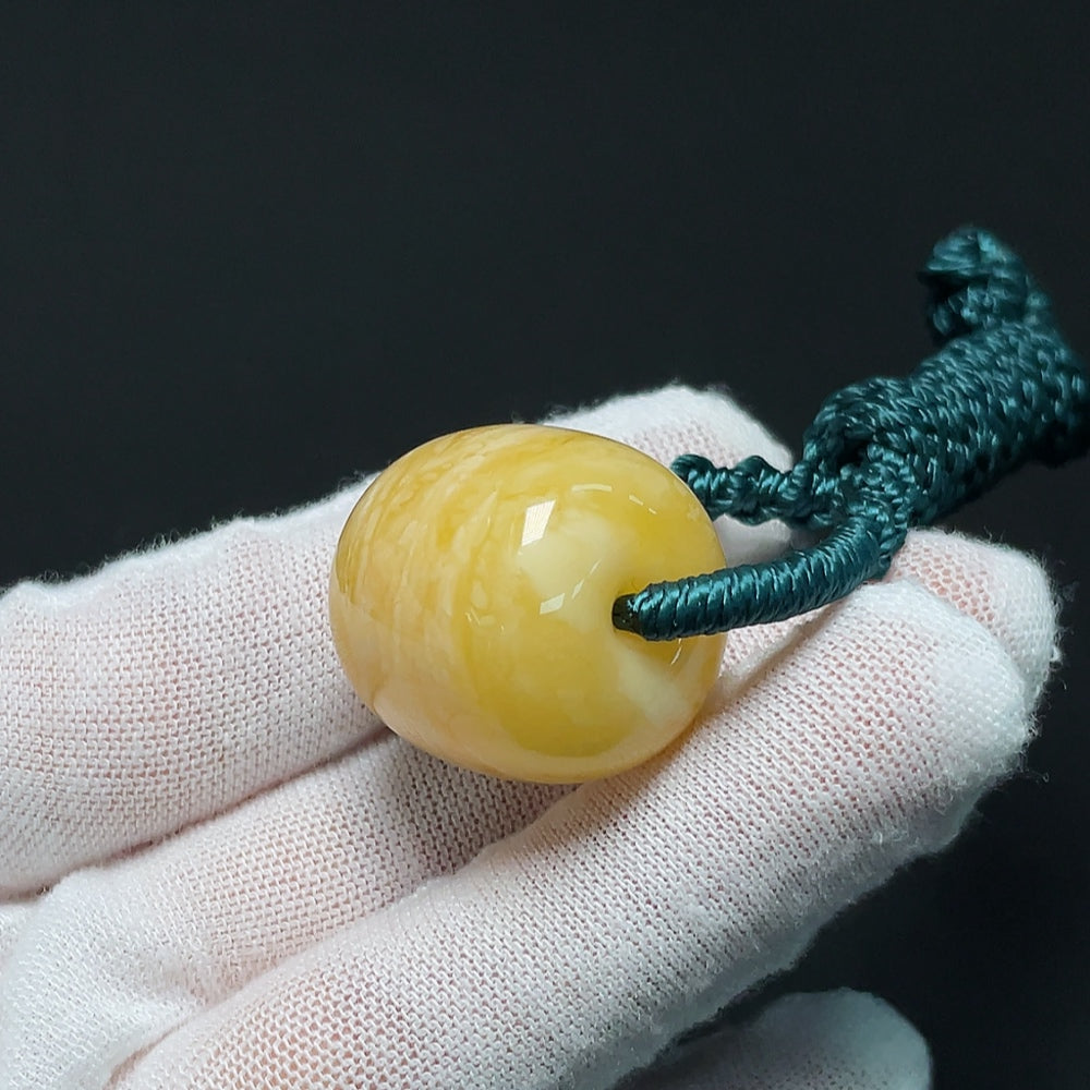 Amber beeswax pendant from HKHQ featuring a natural amber stone with a cord, weighs approximately 10.99 grams.