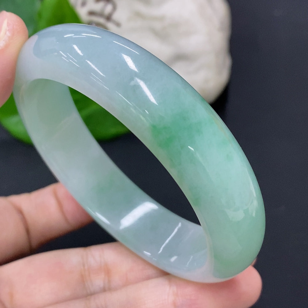 Close-up of HKHQ jadeite round bangle showcasing smooth, polished green jade with intricate natural patterns on a white background.