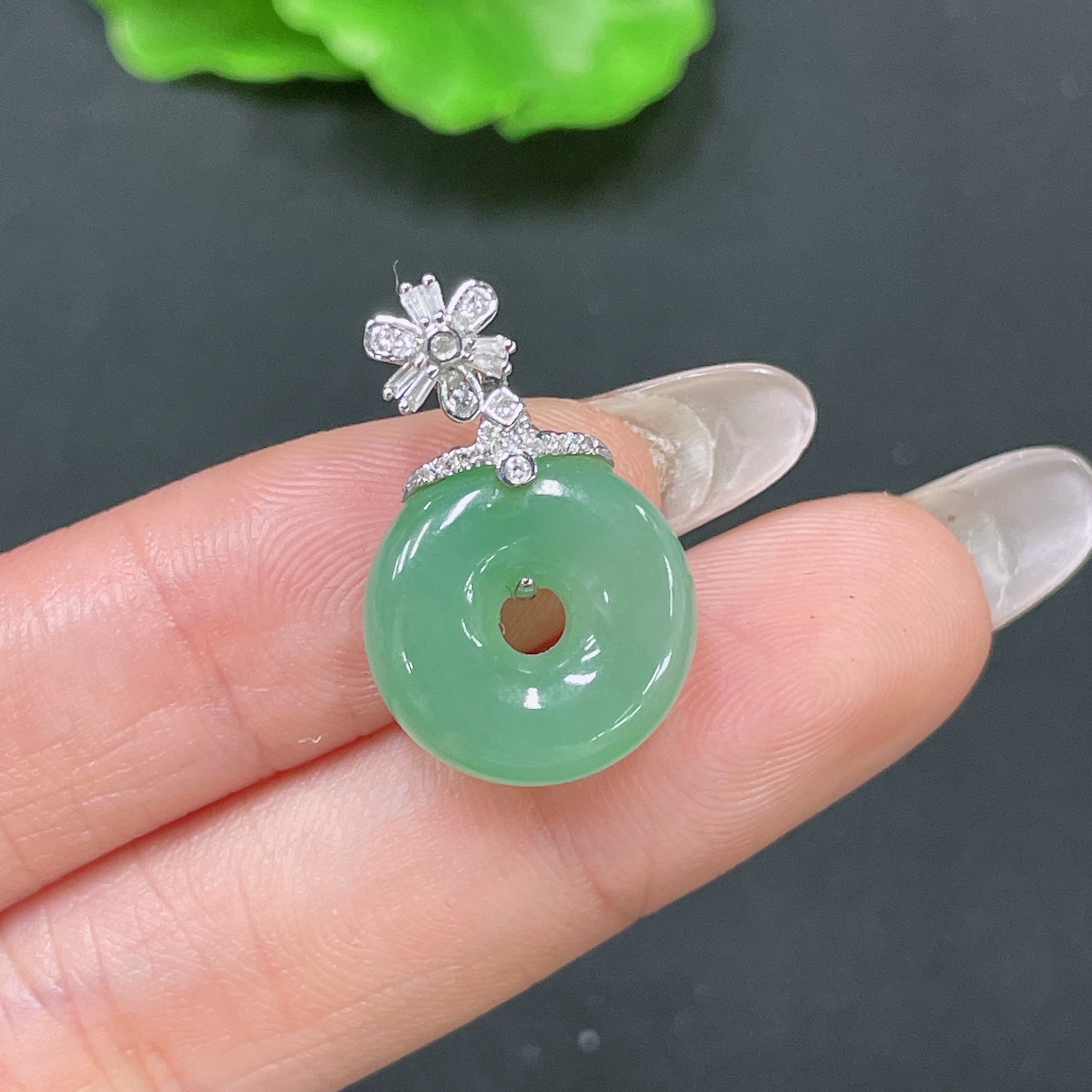 Jadeite pendant with peace knot design, 18k gold inlaid with diamonds, crafted by HUILIU HQ, on a jewelry display.