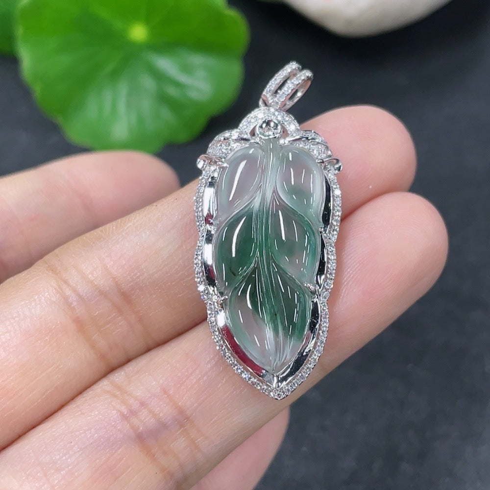 Jadeite leaf pendant with 18K gold accents and diamond details, showcasing a delicate design on a jewelry display.