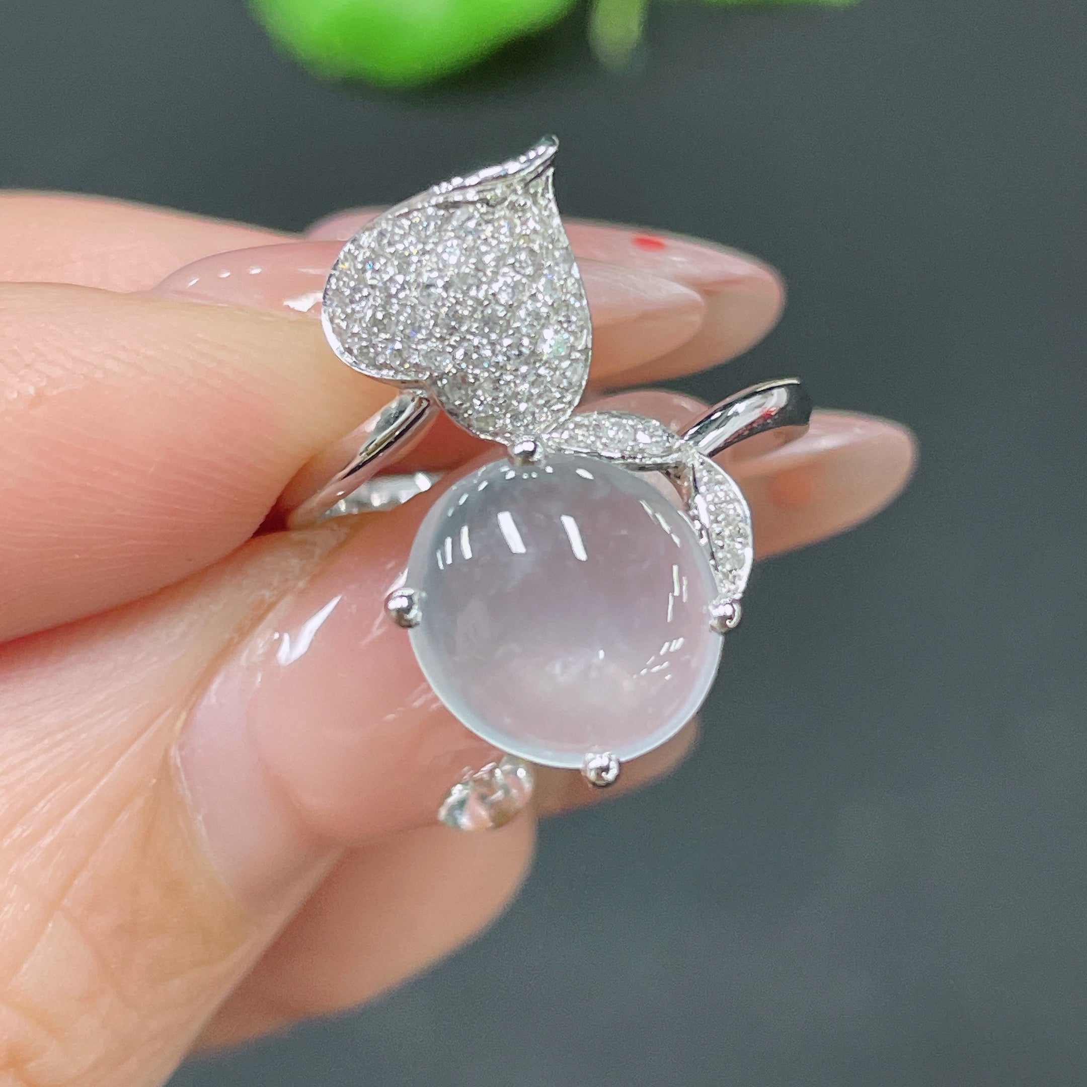 Jadeite cabochon ring with 18k gold band and diamond accents, size 12, worn on a finger with a decorative background.