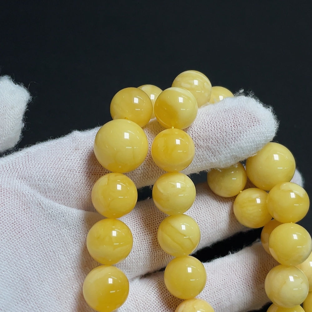 Amber beeswax bead strand with visible repairs, 11.4-14mm, HKHQ brand, weighs approx. 60.86g, showing natural imperfections and color variations.