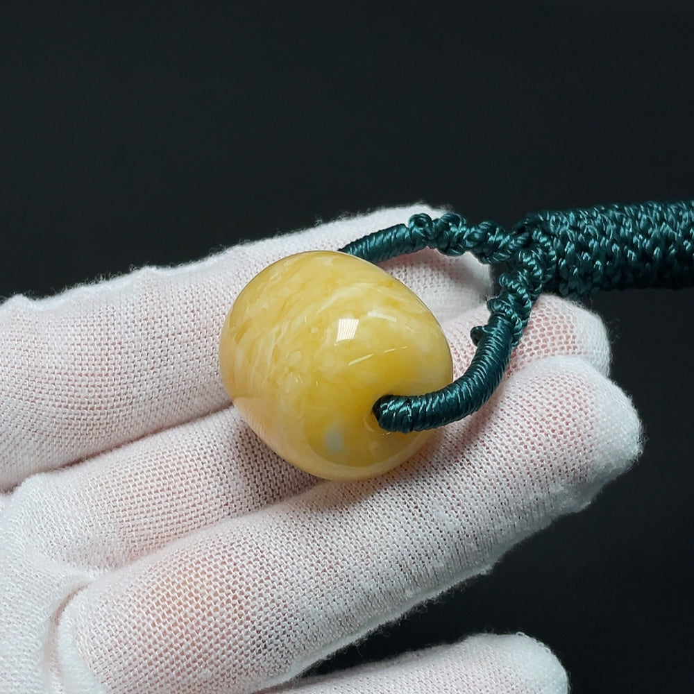Amber beeswax pendant with natural amber hue, attached to a cord, weighing approximately 10.99 grams, by HKHQ.