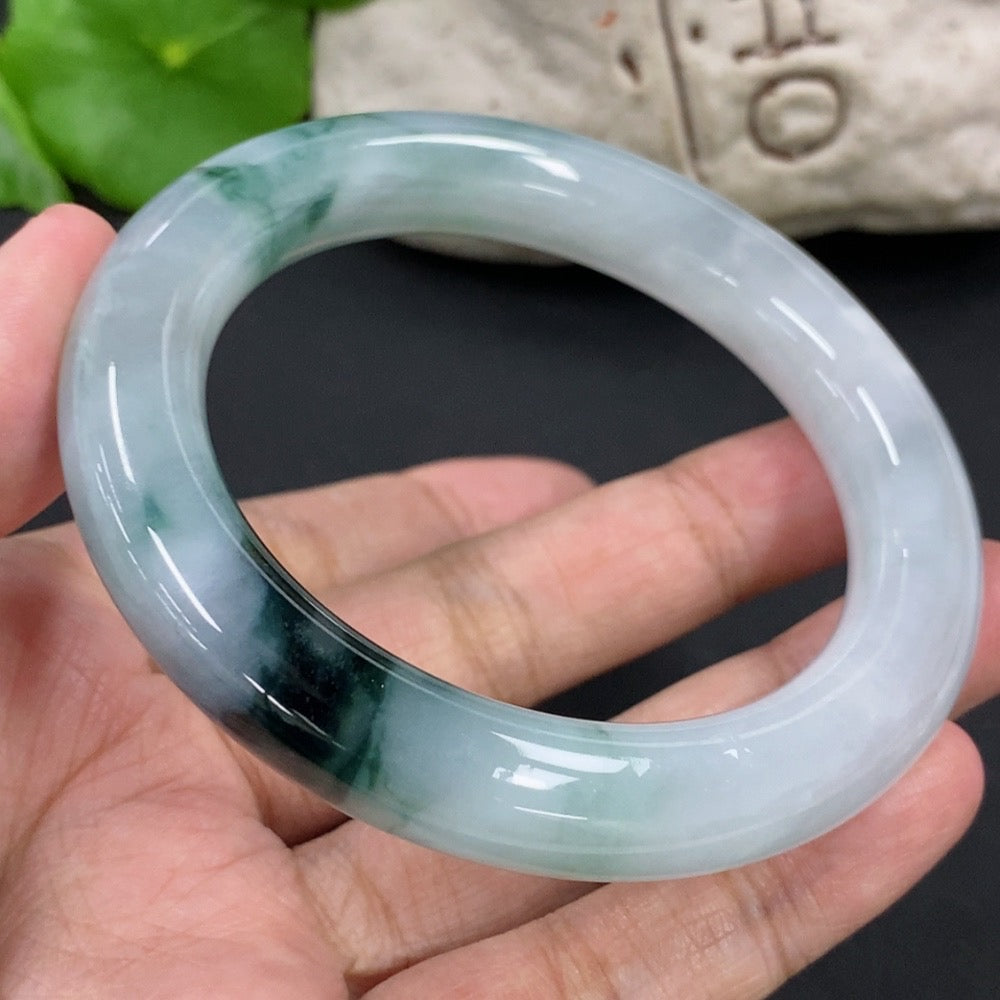 HKHQ jadeite round bangle, size 54.9, with mineral components, showcasing smooth, polished jade surface in natural light.